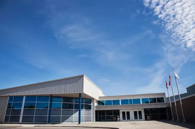 A modern, single-story building with large windows under a clear blue sky. Three flags are flying on poles, adding a sense of formality.