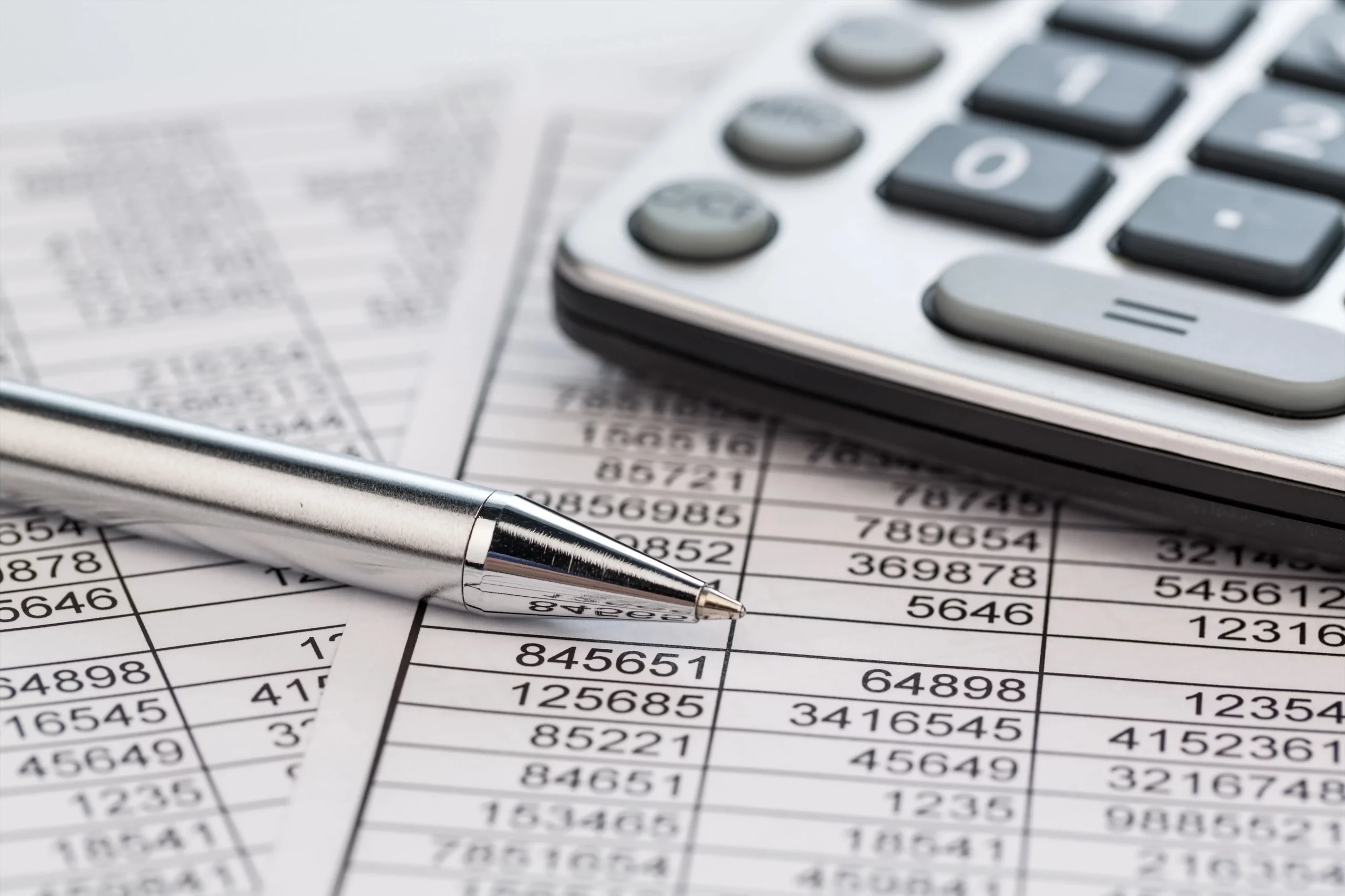 A silver pen and a calculator rest on a sheet filled with numbers and financial data, conveying themes of accounting, budgeting, and analysis.