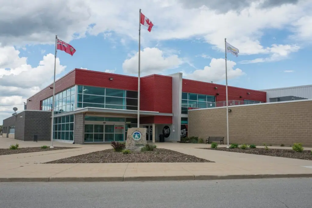 A modern building with red and gray brick, large windows, and three flagpoles flying flags. The sky is partly cloudy, creating a calm atmosphere.